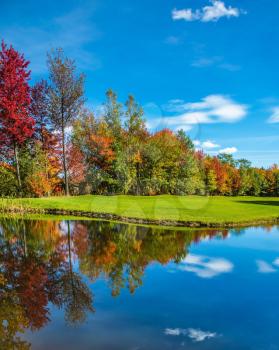  Park of fantastic beauty. Concept of Golf tourism. Golf Club on the road to Bromont, French Canada. Red, orange and green autumn foliage is reflected to clear water of the lake