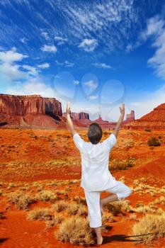 Navajo Reservation in the US. Red Desert and freestanding sandstone cliffs. Woman in white doing yoga