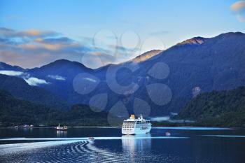 Early morning in the Chilean fjord. Snow-white tourist boat lit rising sun. On the mountains are thin clouds