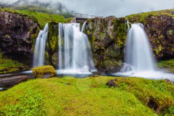 Cloudy day in Iceland. Cascade Falls on the green grassy hill. Mountains and waterfalls