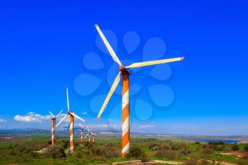 Israel. Several huge modern windmills. Seen in the distance the snow-covered Hermon. Flowering Golan Heights on a sunny day