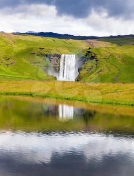  Abounding waterfall Skogafoss reflected in small pond near the road. An incredible reflection