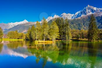 City Park is illuminated by the setting sun. The mountain resort of Chamonix, Haute-Savoie. The lake reflected the snow-capped Alps and evergreen spruce