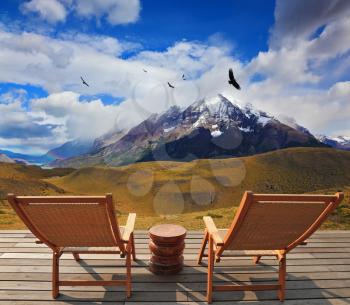 Pleasant holiday. Chile. Wooden chairs in the park Torres del Paine. On the horizon is visible snow-covered rocky mountain