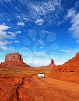  On the road between outcrops of red sandstone - white car. Monument Valley in the Navajo Indian Reservation. Arizona, USA