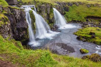 Cascade deep falls Kirkyyufell Foss on the grassy mountains. Iceland - the country of mountains, the rivers and falls