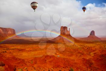 The picturesque rainbow crosses some rocks - mitts. Two huge balloons flies over Red Desert Navajo, USA. On the road is a white jeep