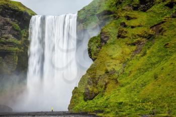 The most popular waterfall in Iceland - Skogafoss. Water rushes down with a crash, forming a cloud of mist. Picturesque huge rainbow appears in the water mist