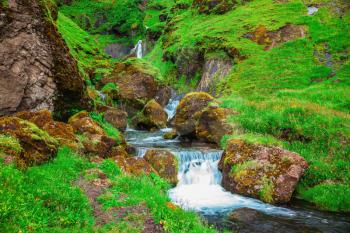 July in Iceland. Basalt mountains overgrown with green grass and moss. Picturesque cascade step falls