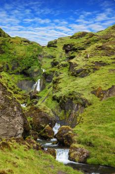 Basalt mountains covered in green moss and grass . Gorgeous cascading waterfall from melting glacier. Iceland, July