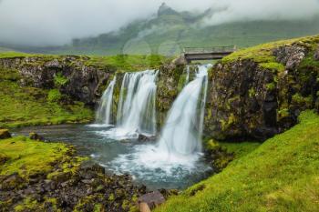 Threaded full-flowing waterfall on the grassy mountains. Iceland - country of mountains, rivers and waterfalls