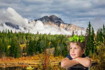 Jasper National Park in the Rocky Mountains of Canada. The yellow and orange autumn grass and trees. Picturesque mountains and clouds. Handsome boy with bright eyes sitting riding on a chair