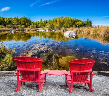 Lovely place. Two red beach chairs on the riverbank. Cirrus clouds are reflected in the Winnipeg River. Old Pinawa Dam Park. The concept of ecological and recreational tourism