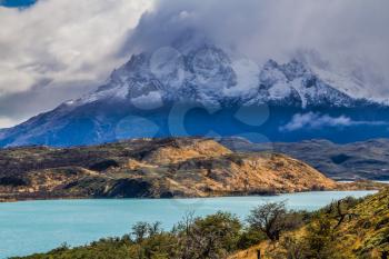 The magnificent cliffs of Los Cuernos in the clouds are covered with snow. Torres del Paine National Park. Summer in the south of Chile. The concept of extreme and active tourism
