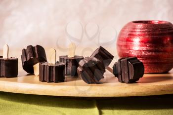 Professional baking. Magnificent portioned chocolate desserts on comfortable wooden sticks. Wooden polished round tray. White background