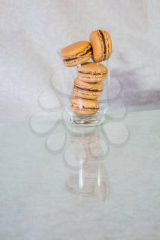 Tall transparent glass with macaroons is reflected in a glass table. Professional bakery