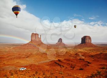 The picturesque rainbow crosses some rocks - mitts. Two huge balloons flies over Red Desert Navajo, USA. On the road is a white jeep