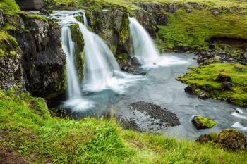 Concept of exotic and extreme tourism. Cascading waterfall Kirkjoufellfoss at the foot of the mountain Kirkjoufell. Summer in Iceland