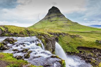 Iceland - the country of mountains, the rivers and falls. Cascade deep falls Kirkyyufell Foss on the grassy mountains
