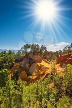 Green trees create contrast with the ocher. Roussillon, Provence Red Village. Multi-colored ocher outcrops - from yellow to orange-red