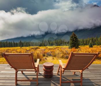 Magnificent multi-colored fall in the Rocky Mountains of Canada. On a wooden scaffold there are two wattled chaise lounges