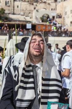 JERUSALEM, ISRAEL - OCTOBER 12, 2014: The area in front of Western Wall of  Temple filled with people.   Young boy in tallit praying. Morning autumn Sukkot