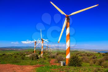 Israel. Flowering Golan Heights on a sunny day. Several huge modern windmills. Seen in the distance the snow-covered Mount Hermon