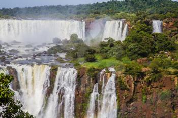Powerful two-stage waterfall creates a watery dust and a rainbow. Several waterfalls from Iguazu Falls. The concept of exotic and extreme tourism