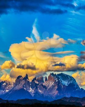 Snow-covered black rocks of Los Cuernos. Magnificent orange clouds in the rays of the sunset. The concept of extreme and active tourism. Torres del Paine National Park