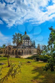 The dome of basilica is surrounded by gallery with columns. Church Sermon on the Mount - Mount of Beatitudes. Subtle shade of palms 