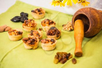 Professional baking. Portioned tartlet cakes with filling of candied nuts and dried fruits. Background wooden mortar with pestle