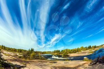 Thin flying cirrus clouds over narrow and rough Winnipeg River, Old Pinawa Dam Park. On the shore is a wooden bench for tourists. The concept of ecological  tourism