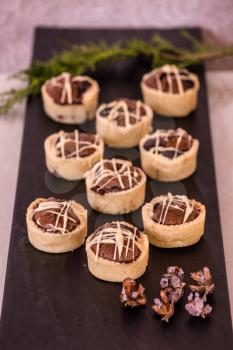 Professional baking. Magnificent portioned tartlet cakes  with chocolate filling. Background black