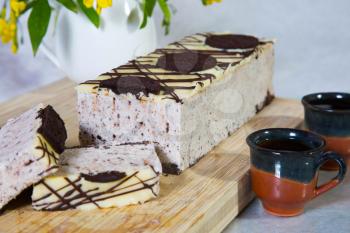 Delightful cheesecake with Oreo cookies. Background - wooden board and ceramic cups. Professional bakery