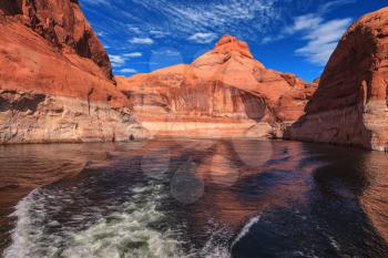 The foamy trace from powerboat crosses emerald waters. The lake Powell on  river Colorado. Hills from red sandstone surround the lake