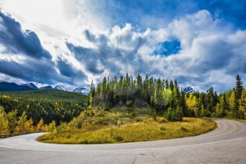The dramatic storm clouds over the Rocky Mountains. The road bends sharply in the woods. The concept of active tourism