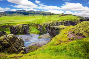 The concept of active northern tourism. The striking canyon in Iceland. Bizarre shape of cliffs surround the stream with glacial water. Green Tundra in summer