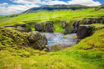 Green Icelandic Tundra in July. Fast river with glacial water flows among cliffs. Magic canyon Fyadrarglyufur. The concept of active northern tourism