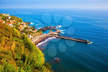 The picturesque village with tiled roofs on the cape is surrounded by forest. The magical tropical island of Madeira. Concept of exotic and ecological tourism