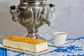  Gorgeous white cheesecake, sprinkled with sweet crumbs. Professional bakery. The background is a  samovar and porcelain cup with hot tea on blue kitchen towel