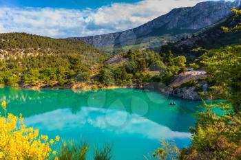 Smooth emerald green river water reflects the sky and wooded shore. Mountain canyon Verdon in the French Alps