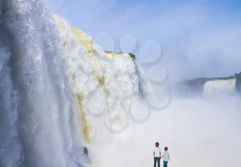 Two boys watch the Iguazu Falls. The world of roaring water. Concept of active and ecotourism