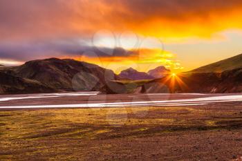 The July morning in the National Park Landmannalaugar, Iceland. Mountains and glaciers covered with warm pink and orange sun