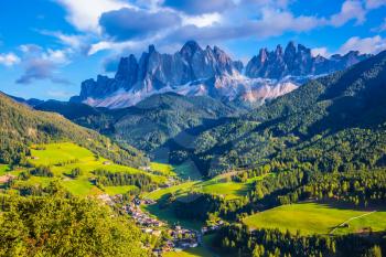 The sun illuminates grandiose crenellated rocks of Tirol, green valley and small picturesque village. The Dolomites. The concept of eco-tourism in Alpine meadows