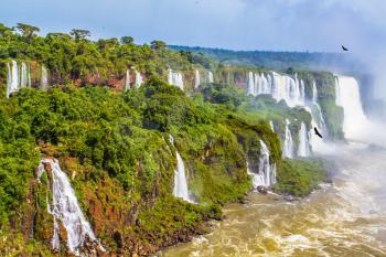 Border of Argentina, Brazil and Paraguay. The most full-flowing waterfalls Iguazu. Andean condors fly in the water dust. Concept of active and extreme tourism