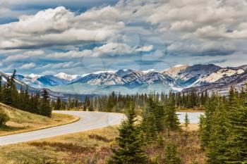 The road to distant snow-capped mountains. Indian summer in the Rockies of Canada. Rocks and lakes under flying clouds. Concept of active and ecological tourism