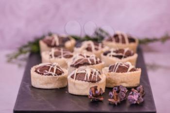 Magnificent portioned tartlet cakes with chocolate filling. Professional baking. Background black