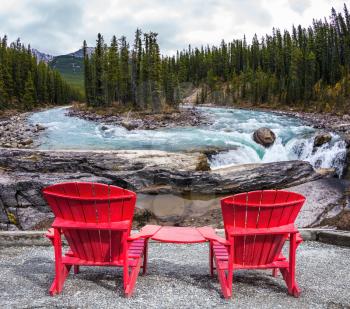 Two red deckchairs stand on the shore of the river. Jasper National Park, Canada. Small island in the middle of the river. The concept of extreme and ecological tourism