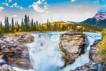 The concept of extreme and ecological tourism. The waters of a melting mountain glacier feed the booming waterfall of Athabasca. Travel to Jasper Park, Canada. Clear autumn evening at sunset