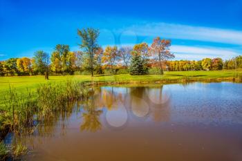 Autumn foliage reflected in small oval pond  with clay bottom. Shining sunny day in French Canada. Concept of recreational tourism